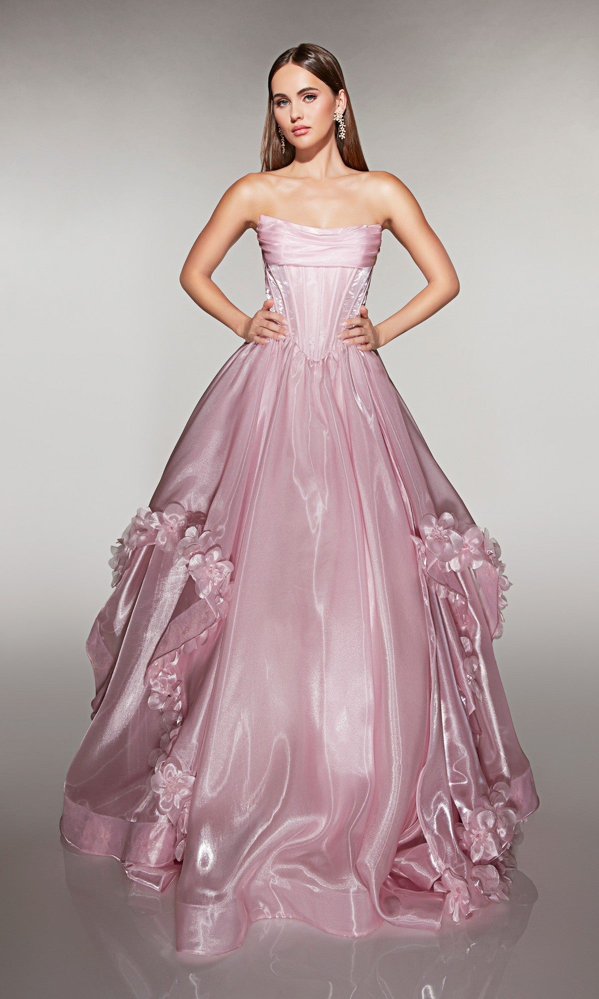 A woman poses in the Alyce 62014 long prom dress, a strapless ballgown with a shiny, voluminous light pink liquid organza skirt and 3D floral appliques.